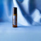 A small amber glass roller bottle with a black cap and a white label reading 'doTERRA DigestZen Touch DigestZen' stands on a smooth blue surface against a softly draped blue background.