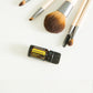 A set of makeup brushes with light wood handles and silver ferrules arranged on a white surface, alongside a small black doTERRA essential oil bottle labeled Decadentia. doTERRA Helichrysum Essential Oil