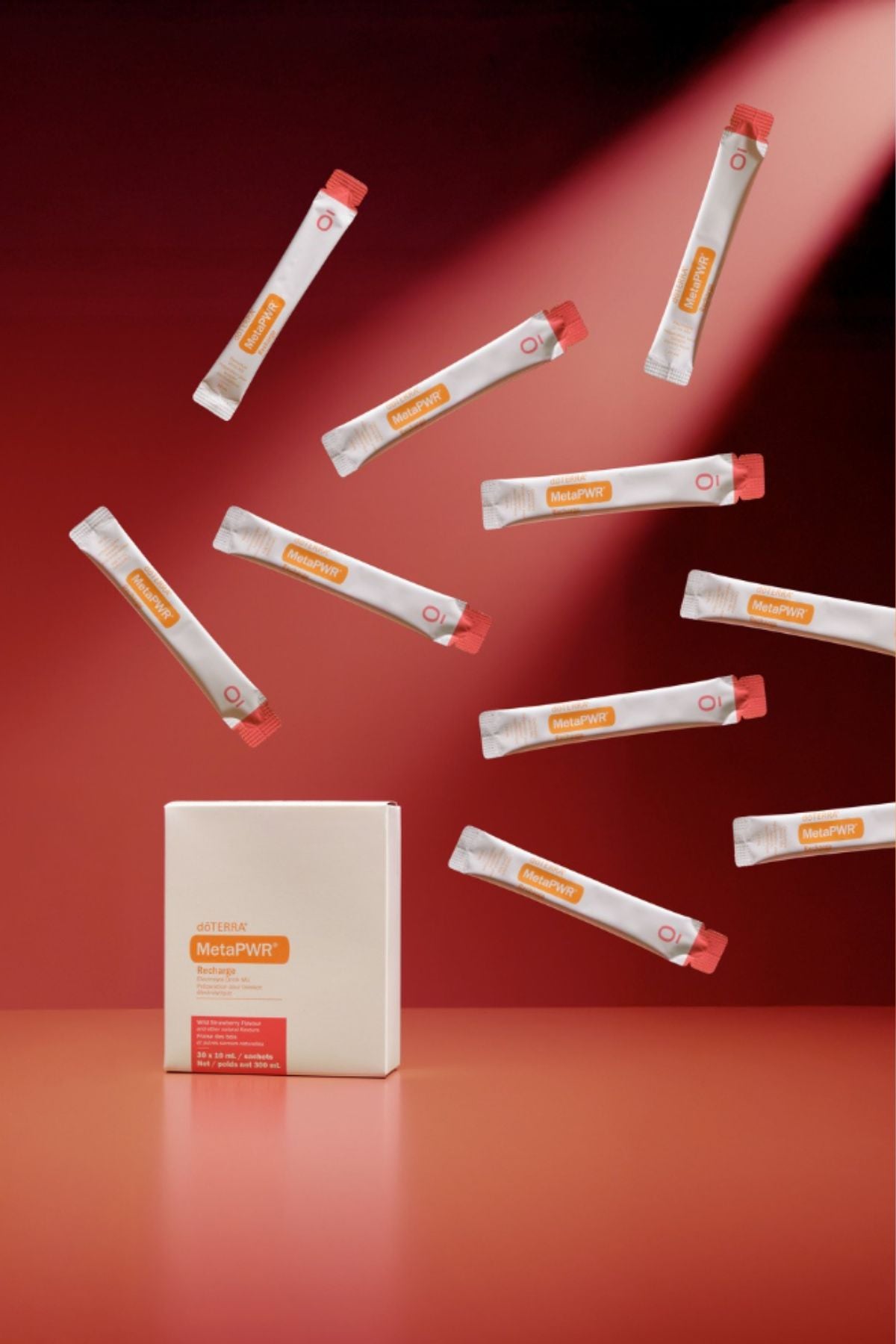 A white rectangular box labeled MegaPWT stands on a red surface, with multiple white single-serve packets floating around it against a red studio background. MetaPWR Recharge Electrolytes - Wild Strawberry