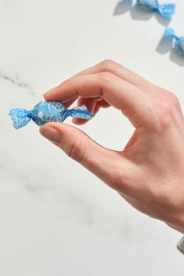 Hand holding a blue-wrapped candy against a light background