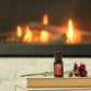 A small bottle of doTERRA Harvest Spice placed on a stack of books in front of a warm fireplace, with a flower resting beside it.