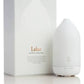 A white essential oil diffuser bottle standing next to its white packaging box, which features the brand name 'Laluz' in gold text. dōTERRA LaLuz Diffuser