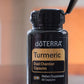 A bottle of doTERRA Turmeric Dual Chamber Capsules with a black cap and label, shown on a reflective surface with a few yellow capsules in front against a warm blurred background.