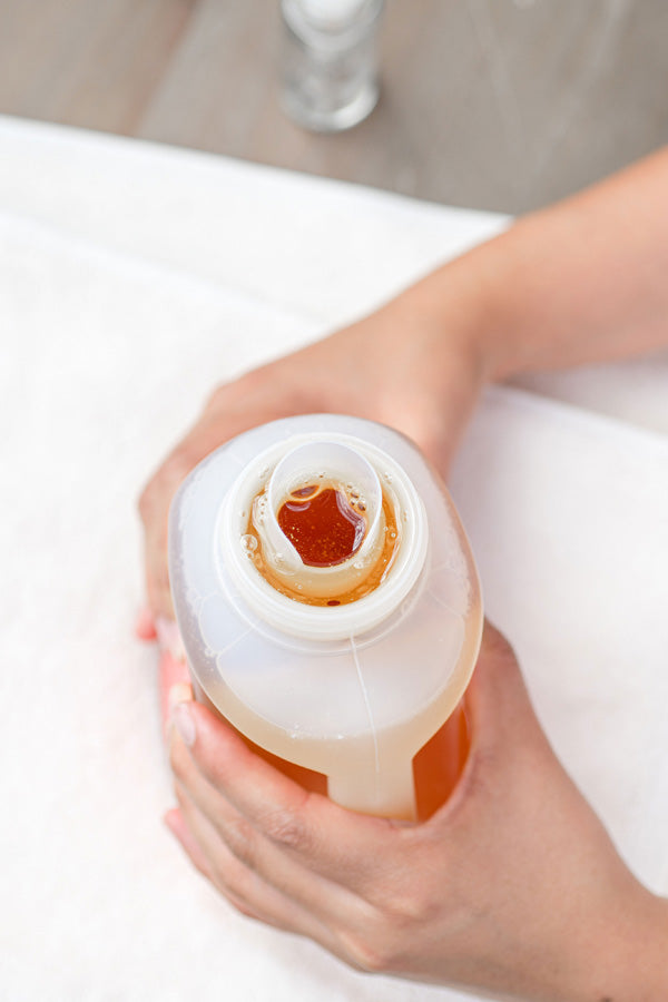 Hand holding a bottle of liquid with a white cap on a light background